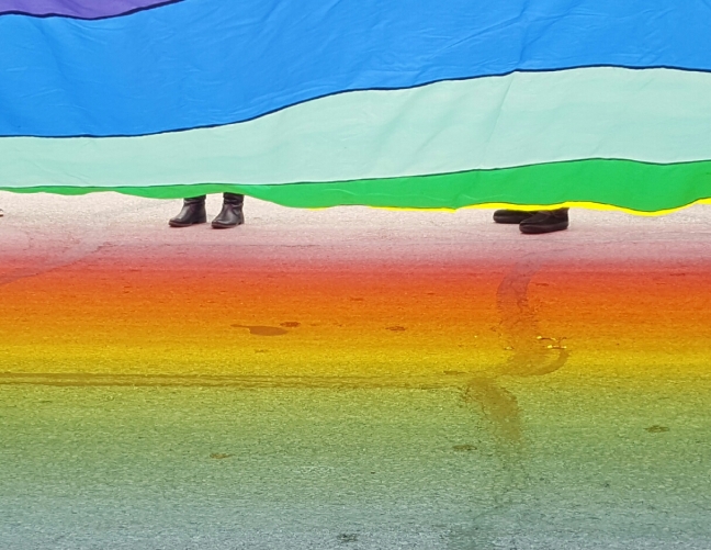 The sun reflects a rainbow on the pavement underneath a large rainbow flag carried by members of Heartland Pride, who marched in the St. Patrick's Day Parade in downtown Omaha on March 11. EMMA WHALEY/EXPLORING